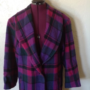 Pode incluir: Um casaco comprido xadrez em tons de roxo, rosa, verde e preto. O casaco é exibido em um manequim e apresenta uma gola larga e um fecho de um botão. O tecido parece ser uma mistura de lã.
