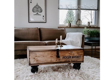 May include: A wooden coffee table with wheels, featuring a distressed wood finish and a black metal latch. The table has a label that reads "No. 3 Old Style JACKSON WHISKEY DISTILLED & BOTTLED TENNESSEE USA".