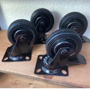 Pode incluir: Quatro rodízios giratórios pretos com placas de metal. Os rodízios têm uma roda de borracha preta e uma estrutura de metal.
