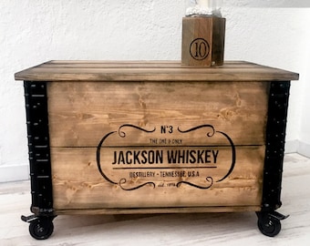 May include: A wooden storage box with black metal accents and wheels. The box has a label that reads "N°3 THE ONE & ONLY JACKSON WHISKEY DESTILLERY TENNESSEE, U.S.A est. 1898".