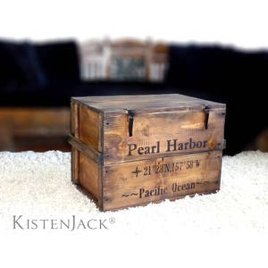 Peut inclure: Une boîte de rangement en bois avec un couvercle à charnières et des fermoirs métalliques. La boîte est décorée du texte "Pearl Harbor" et des coordonnées "21 28°N,157°58 W" ainsi que du texte "~~Pacific Ocean~~".