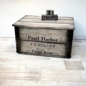 May include: A wooden storage box with metal accents and the words "Pearl Harbor" and "~Pacific Ocean~" printed on the front. The box is sitting on a light wood floor.