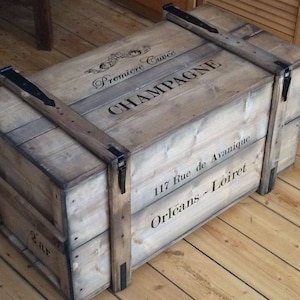 Op de afbeelding: Een houten opbergkist met zwarte metalen scharnieren en een label met de tekst "Premiere Cruce Champagne 117 Rue de Avanique Orleans - Loiret".
