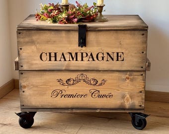 Puede incluir: Un cofre de almacenamiento de madera con ruedas, con el texto "Champagne Premiere Cuvee" y un cierre de metal negro. El cofre está decorado con una corona de flores y velas.