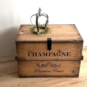 May include: A wooden champagne chest with the word "CHAMPAGNE" printed on the front. The chest has a decorative metal crown on top. The words "Premiere Cuvee" are printed on the front of the chest.