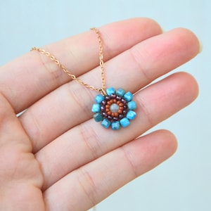 This dainty pendant is inspired by ancient Roman mosaics and pictures a little flower. The colours are white/light blue in the centre, and orange/brick, purple and blue in the outer layers. The chain is rose gold, and less than 1 millimetre thick.