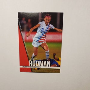 May include: A trading card featuring Trinity Rodman, a football player for the US Women's National Team. The card is red, white, and blue with the text "2020 Hot Shot Prospects".