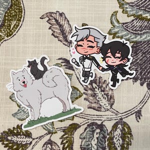 May include: Three stickers featuring cartoon illustrations. One shows a white dog with a black cat on its back. Another depicts two cartoon figures holding hands. The third sticker shows two cartoon figures holding hands.