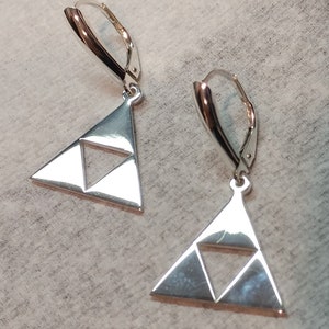 Puede incluir: Un par de pendientes de plata con un diseño triangular. Los triángulos tienen un triángulo más pequeño en el interior, creando un efecto tridimensional.