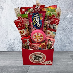 May include: A red box filled with an assortment of candies, including Nerds Gummy Clusters, Sour Patch, and Ring Pop. A pink flower-shaped item is in the center. The box has a Camp Pontiac logo.
