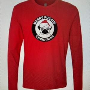 May include: Red long-sleeve t-shirt with a black and white circle graphic featuring a pug wearing a Santa hat. The text "Merry Puggin' Christmas" is inside the circle.