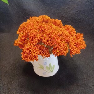 May include: A bouquet of dried orange marigold flowers in a white ceramic pitcher with a blue floral design.