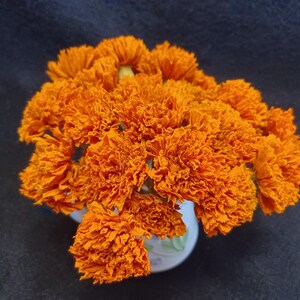 May include: A bouquet of bright orange marigold flowers arranged in a white vase with a floral pattern.