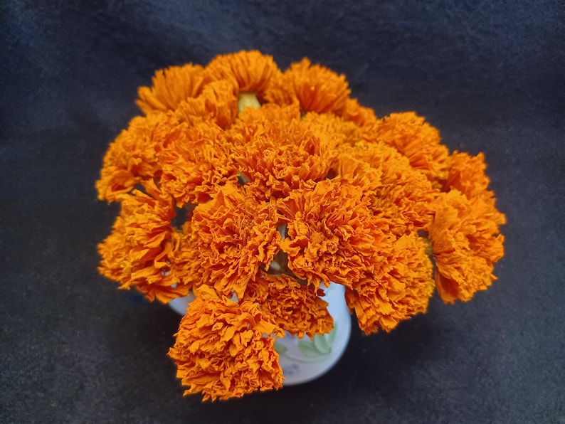 May include: A bouquet of bright orange marigold flowers arranged in a white vase with a floral pattern.