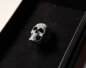 Peut inclure: Une petite figurine de crâne blanche et détaillée dans une boîte en velours noir.