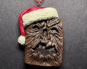 May include: A brown and white Christmas ornament shaped like a creature with a scary face wearing a red and white Santa hat.