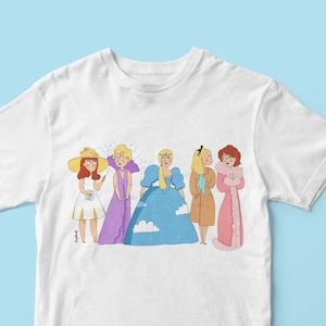 Peut inclure: T-shirt blanc avec un imprimé graphique de cinq femmes dans différentes tenues. Les femmes sont debout en ligne et sourient toutes. Le graphique est dans un style cartoon.