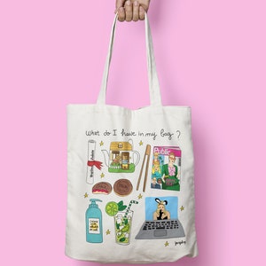 May include: A white tote bag with a hand-drawn illustration of various items, including a house, a teapot, a magazine, a laptop, a glass of lemonade, a diploma, chopsticks, and cookies. The text "What do I have in my bag?" is written at the top of the bag.