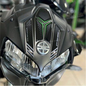 Può includere: Primo piano di una moto nera con un pad per serbatoio in fibra di carbonio verde e nero. Il pad per serbatoio ha il testo "MOTO STYLING TEAM" e "BLACK DOVES CONCEPT" stampato su di esso. La moto ha un emblema argentato con la lettera "S" all'interno di un cerchio.
