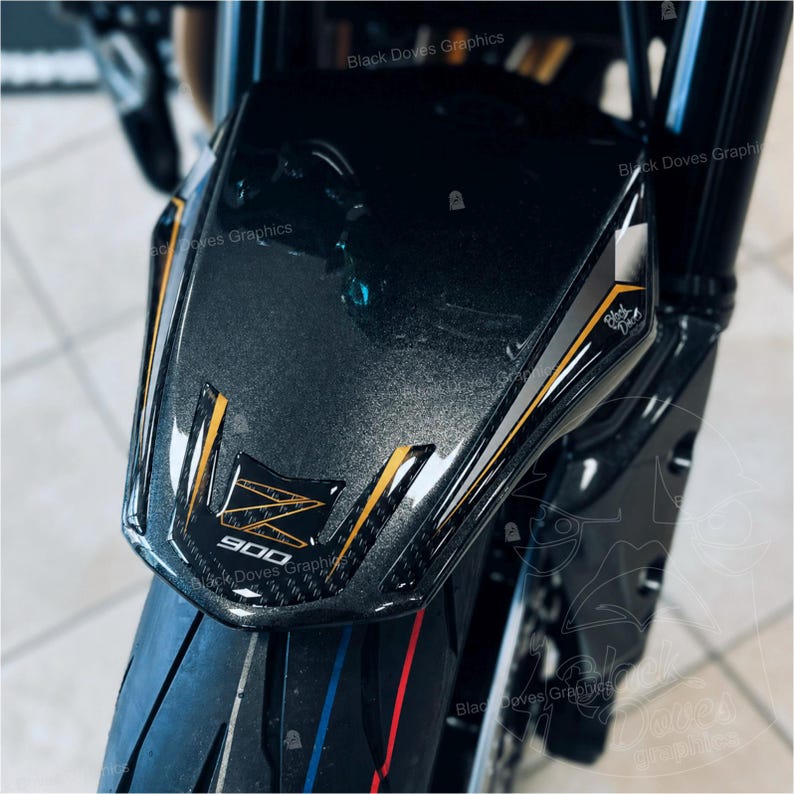 Pu&ograve; includere: Primo piano di un parafango anteriore di una moto. Il parafango &egrave; grigio scuro con accenti dorati e neri. Il testo "900" e una "Z" stilizzata sono visibili. Lo pneumatico ha strisce rosse e blu.
