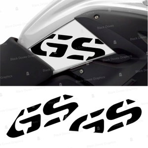 Può includere: Adesivo bianco e nero con le lettere "GS" ripetute tre volte. L'adesivo è progettato per essere applicato su una motocicletta.