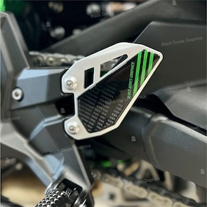 Può includere: Primo piano di una moto con un adesivo in fibra di carbonio nero e verde sul lato. L'adesivo ha il testo "BLACK DOVES GRAPHICS".