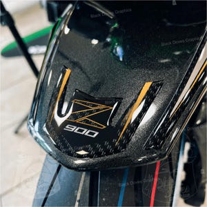 Pu&ograve; includere: Primo piano di un cupolino nero per moto con dettagli dorati e bianchi. Il cupolino presenta il numero "900" in bianco e il testo "Black Doves Graphics". La superficie ha un aspetto strutturato e maculato.