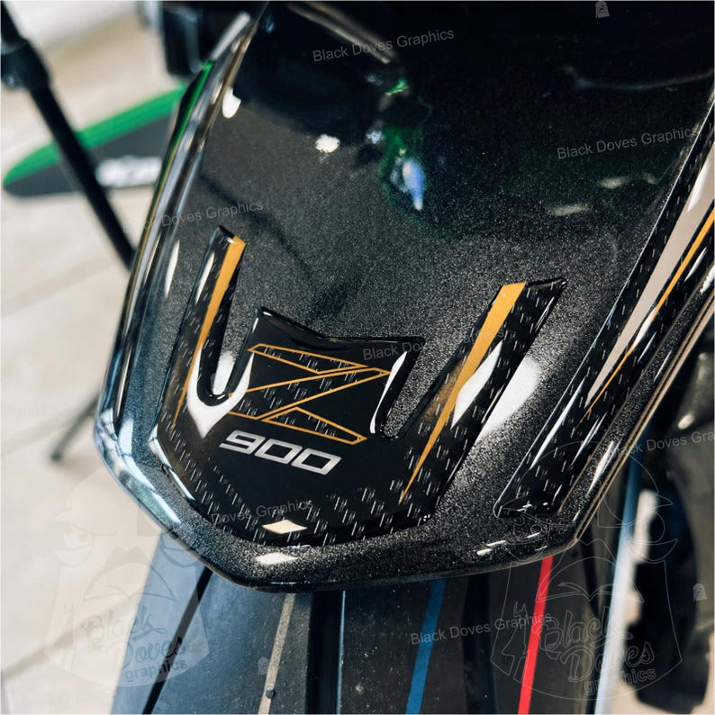 Pu&ograve; includere: Primo piano di un cupolino nero per moto con dettagli dorati e bianchi. Il cupolino presenta il numero "900" in bianco e il testo "Black Doves Graphics". La superficie ha un aspetto strutturato e maculato.