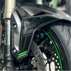 Può includere: Primo piano di un parafango di una moto con un design in fibra di carbonio nero e verde. Il parafango ha la scritta "CKIBSO" stampata su di esso. La ruota della moto ha una striscia verde attorno al cerchio.