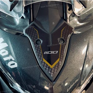 May include: Close-up of a motorcycle's front fairing. The fairing is primarily gray with a black and yellow accent piece. The text "1100" is displayed in white. The words "Black Doves Graphics" are repeated throughout the image.