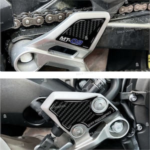 Może przedstawiać: Zbliżenie na podnóżek motocykla z czarną naklejką z włókna węglowego z napisem "BLACK DOVES GRAPHICS".