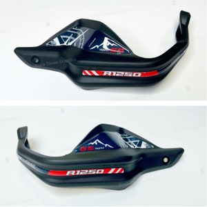May include: Black motorcycle handlebar hand guards with a red and white stripe and a blue and white graphic that says "GS Trophy" and "R1250".