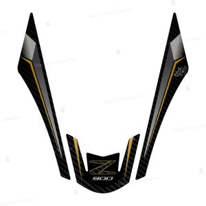 Pu&ograve; includere: Un paraserbatoio per moto nero e oro con una trama in fibra di carbonio. Il design include il testo "Z 900" in oro, con un logo "Z" stilizzato. Il cuscinetto ha una forma unica con bordi angolari e un accento argento metallizzato.
