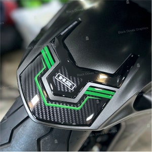 Può includere: Primo piano di un serbatoio di una moto con un motivo in fibra di carbonio e accenti verdi. Il serbatoio ha un logo "H2" in bianco e nero.