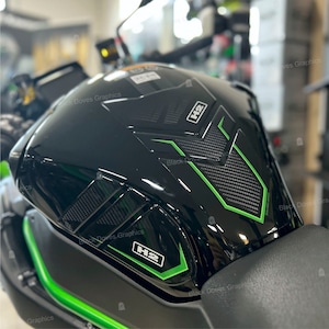 Op de afbeelding: Zwarte motorfiets benzinetank met groene en zwarte grafische accenten. De tank heeft een carbonvezel textuur en de tekst "H2" is op de tank gedrukt.