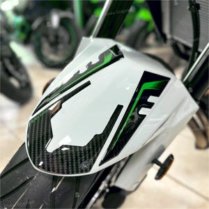 Op de afbeelding: Een witte motorfiets spatbord met zwarte en groene grafische accenten. Het spatbord heeft een koolstofvezelpatroon aan de onderkant en de tekst "BLACK DOVES" is zichtbaar. Het ontwerp bevat zwarte en groene lijnen en vormen.