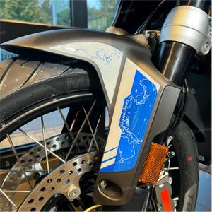 May include: A close-up of a motorcycle fender with a blue and white world map graphic decal. The decal features the text "BLACK DOVES GRAPHICS".