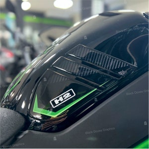 Può includere: Primo piano di un serbatoio di benzina per moto nero con logo H2 verde e bianco e dettagli in fibra di carbonio.