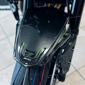 Può includere: Primo piano di un parafango anteriore per moto con finitura nera e grigia. Il parafango presenta strisce verdi e bianche e il numero "900" in un emblema verde e nero. Il testo "Black Doves Graphics" è visibile.
