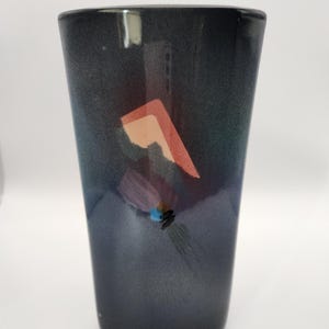 May include: A dark grey ceramic vase with a geometric design in shades of pink, blue, and green.