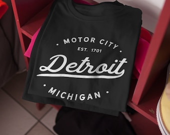 May include: Black t-shirt with white text that reads "Motor City. Est. 1701. Detroit. Michigan."