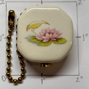 May include: Cream-colored, octagonal ceramic pull chain pendant with a gold-colored chain. The pendant features a yellow bird and pink lotus flower design. The pendant measures approximately 1 inch by 1 inch.