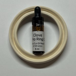 May include: A small amber glass dropper bottle containing 5 ml of Clove Hemp Ring Oil, featuring a black dropper cap and a white label with black text that reads Clove Hemp Ring Oil and Keep Out Of Reach of Children, centered inside a beige ring.