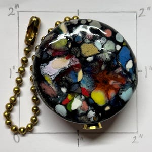 Puede incluir: Una taza de cerámica blanca con asa negra y el texto "But First, Coffee" en negrita negra. La taza se encuentra sobre un fondo borroso, sugiriendo un ambiente acogedor.