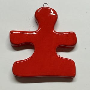 May include: A glossy red puzzle piece ornament with a silver wire loop for hanging. The ornament has a smooth, reflective surface and a classic puzzle piece shape, perfect for holiday decor or as a unique gift.
