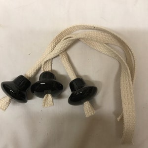 Op de afbeelding: Drie zwarte keramische lamptrekkers met crèmekleurige katoenen koorden. De trekkers hebben een afgeronde bovenkant en een uitlopende basis. De koorden zijn gevlochten en hebben een gerafelde uiteinde. De items staan op een witte achtergrond.