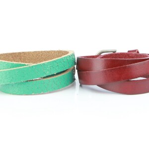 May include: Two leather wrap bracelets. One is a textured green, the other is a smooth burgundy. Both are coiled, showing the inner and outer surfaces. The burgundy bracelet has a silver-tone buckle.