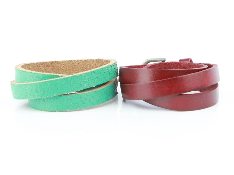 May include: Two leather wrap bracelets. One is a textured green, the other is a smooth burgundy. Both are coiled, showing the inner and outer surfaces. The burgundy bracelet has a silver-tone buckle.