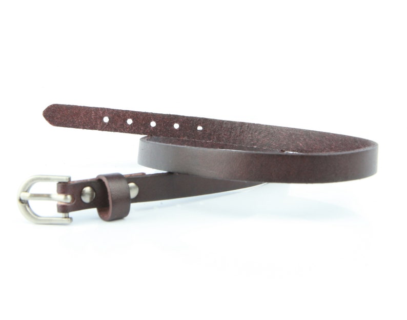 May include: A dark brown leather belt with a silver buckle. The belt is thin and has several adjustment holes. The buckle is a simple, classic design. The belt is likely made of genuine leather.