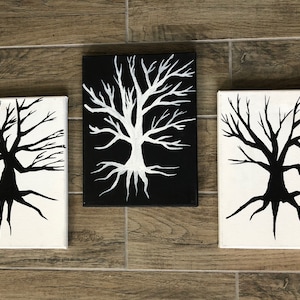 Puede incluir: Tres pinturas de lienzo en blanco y negro de árboles estilizados con ramas y raíces desnudas. Los árboles están pintados en un estilo minimalista, con las ramas y las raíces formando un patrón geométrico simple.